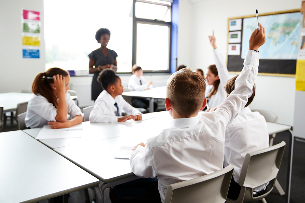 High,School,Students,Wearing,Uniform,Raising,Hands,To,Answer,Question