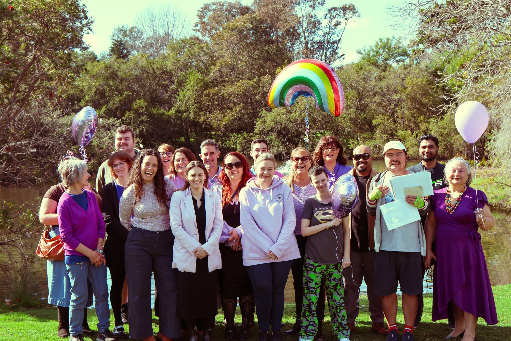 The Interchange Shoalhaven team smiling together outdoors by a lake, holding balloons